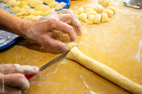 фотографія Closeup shot of floury hands cutting the dough with a knife on a wooden table