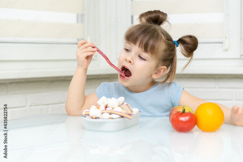 little girl makes a choice between candy and fruit. the child rejects healthy foods and chooses unhealthy foods little girl makes a choice between candy and fruit. the child rejects healthy foods and chooses unhealthy foods