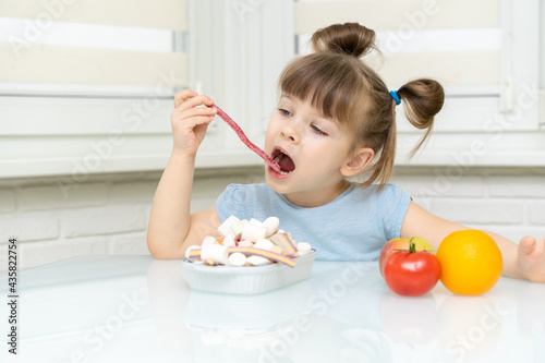 little girl makes a choice between candy and fruit. the child rejects healthy foods and chooses unhealthy foods