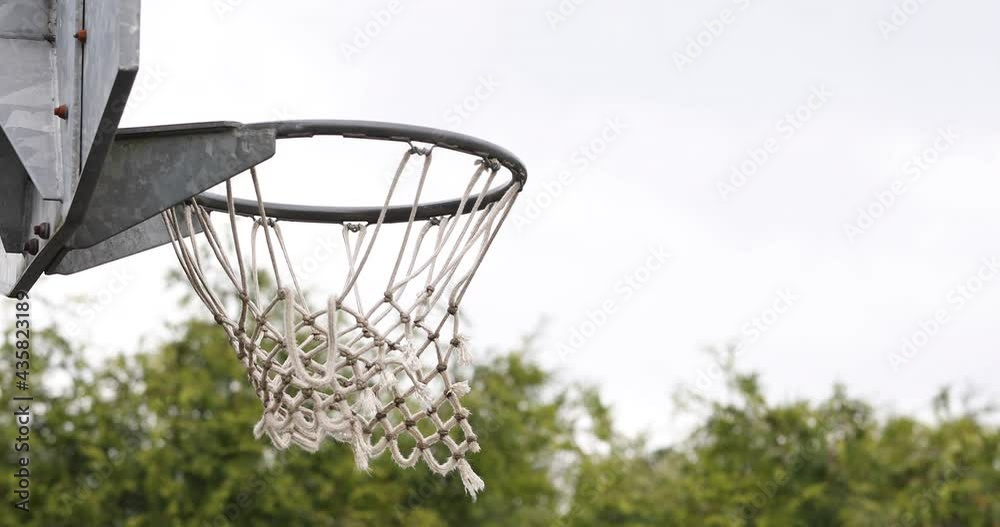 Close shot of basketball hoop as ball goes through the net on an outdoor court Close shot of basketball hoop as ball goes through the net on an outdoor court