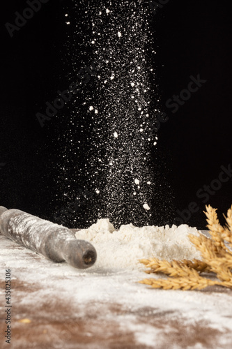 Close-up of flour falling on a pile of flour, on wooden table with wheat, selective focus, black background, vertical, with copy space