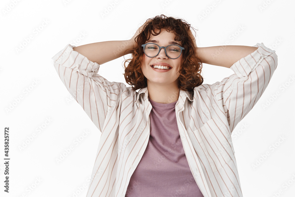 Portrait of happy relaxed girl at her day off. Smiling woman resting, holding hands behind head and looking pleased, enjoying weekend, standing against white background Portrait of happy relaxed girl at her day off. Smiling woman resting, holding hands behind head and looking pleased, enjoying weekend, standing against white background