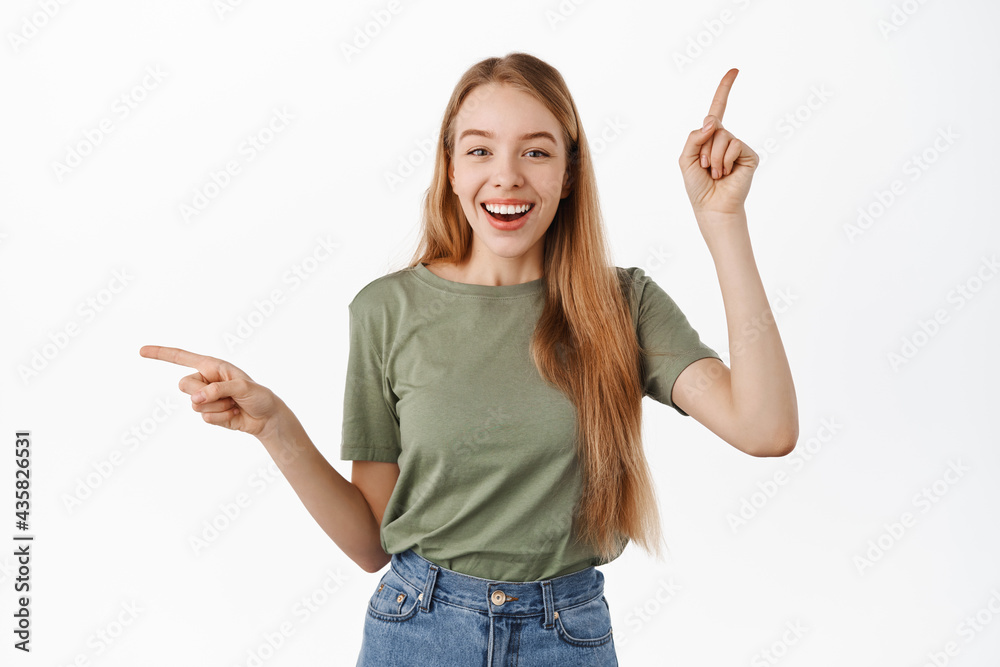 Image of relaxed happy young woman pointing fingers sideways on top and left, smiling and laughing, recommending two products, showing choices, standing over white background Image of relaxed happy young woman pointing fingers sideways on top and left, smiling and laughing, recommending two products, showing choices, standing over white background