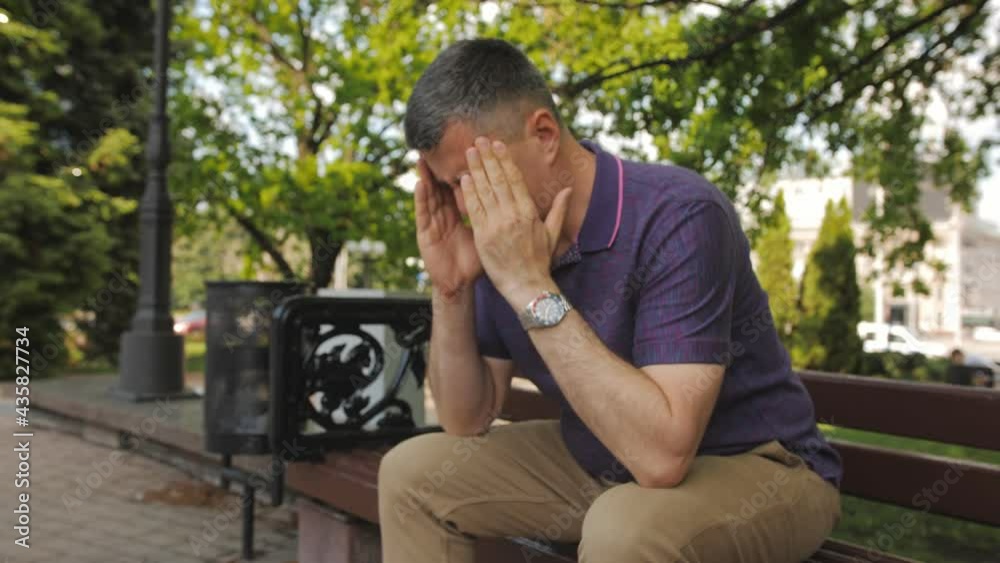 Middle-aged man with headache sitting on bench in city Middle-aged man with headache sitting on bench in city