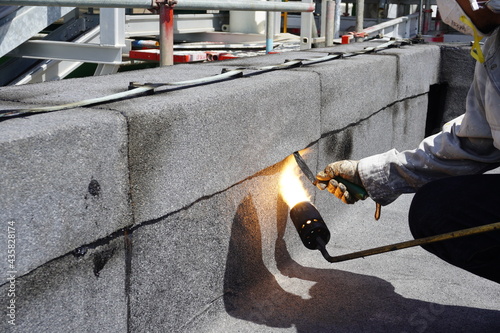 Flat roof installation with propane blowtorch during construction works with roofing felt. Heating and melting bitumen roofing felt.