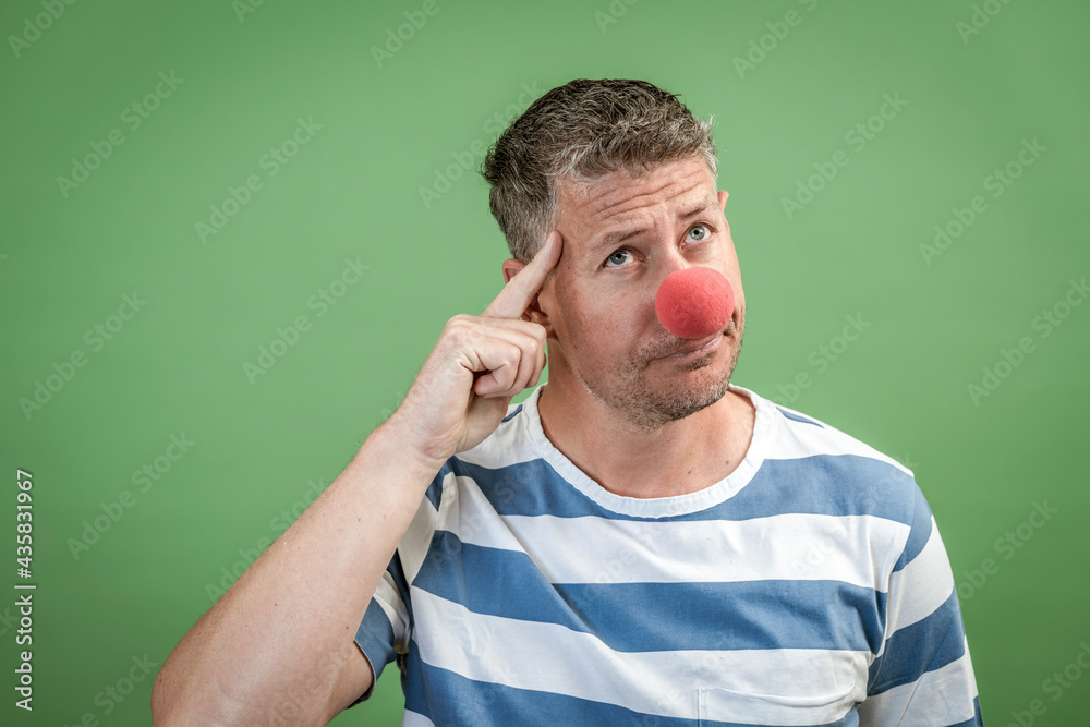 Man with red clown nose and gray hair with blue and white striped shirt stands in front of green background in the studio Man with red clown nose and gray hair with blue and white striped shirt stands in front of green background in the studio