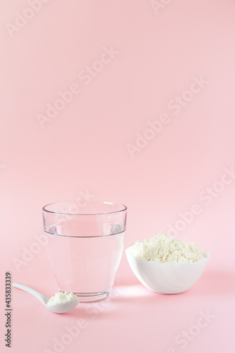 Protein or collagen powder and a glass of water on a pink background with a copy space. Extra protein intake. Food supplement concept. Natural beauty and health supplement. Plant based collagen.