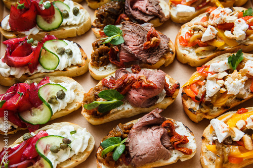 
A set of different snacks for a party or a festive table. Ciabatta sandwiches with tomatoes, jamon, cream cheese, vegetables, chambers and olives. Delicious wine snacks