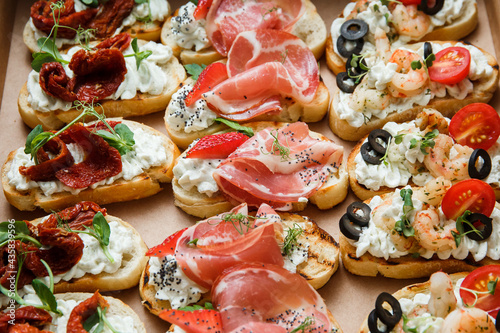  A set of different snacks for a party or a festive table. Ciabatta sandwiches with tomatoes, jamon, cream cheese, vegetables, chambers and olives. Delicious wine snacks