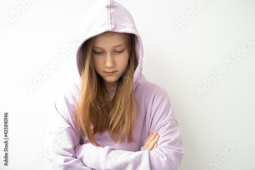 close up hooded upset girl with long hair in purple hoodie standing against white wall photo