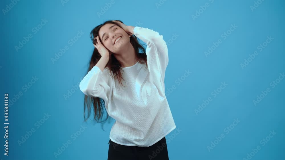The charismatic girl smiles tired with her hands on her head, playing with her hair. Asian with dark hair, dressed in a blue blouse, isolated on a dark blue background in the studio. The lifestyle The charismatic girl smiles tired with her hands on her head, playing with her hair. Asian with dark hair, dressed in a blue blouse, isolated on a dark blue background in the studio. The lifestyle
