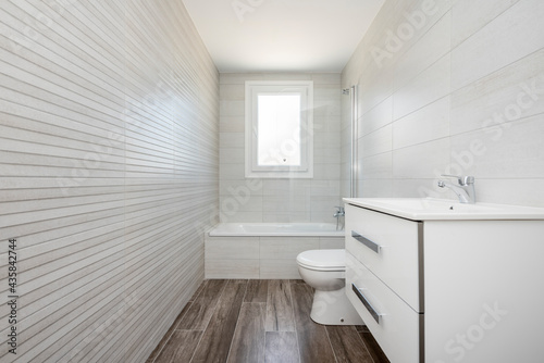 Small white bathroom with bathtub, white cabinet with drawers and sink on the right, with dark ceramic floor