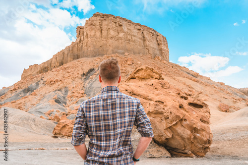 A young man in a plaid shirt stands near a huge valnois with a beautiful view of Alstrom Point, Utah, USA