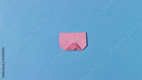 The pig's head is folded from pink paper in the technique of origami with painted mustache. In center of the blue background. Concept of love pets, farm, pastime, hobbies, activities with children.