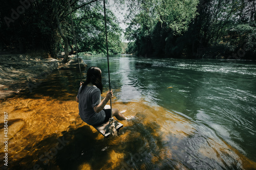 young cute Japanese hipster girl relaxing at beautiful lake view sitting river jungle mountains green forest at Phetchaburi, Kanchanaburi, Thailand. guiding idea women backpacker