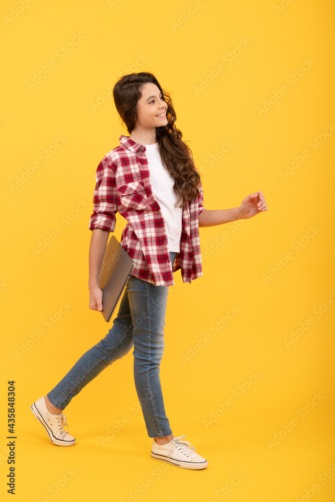 Happy kid go to school holding laptop computer digital device yellow background, learning technology