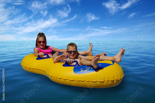 Boy and girl on inflatable float in blue sea water. © Alekss