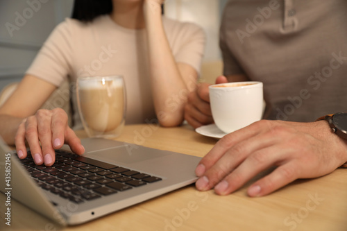 Couple with coffee and laptop at cafe in morning, closeup