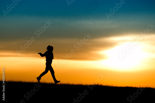 Silhouette of girl running in sunset. © Mihai