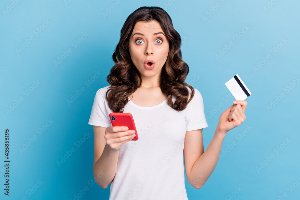 Photo of funny impressed young woman wear white t-shirt holding modern device credit card smiling isolated blue color background Photo of funny impressed young woman wear white t-shirt holding modern device credit card smiling isolated blue color background