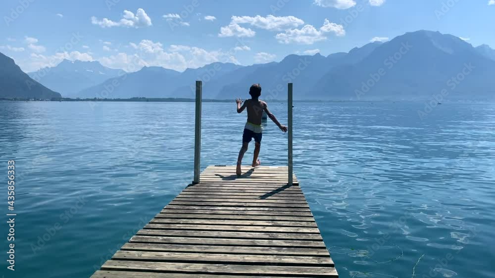 Young boy running by lake pier and jumping into water. child runs at pier and dives into lake Young boy running by lake pier and jumping into water. child runs at pier and dives into lake