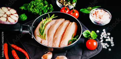 Chicken fillet in a skillet with spices and vegetables on a dark background. Raw chicken meat cut into pieces for cooking. photo