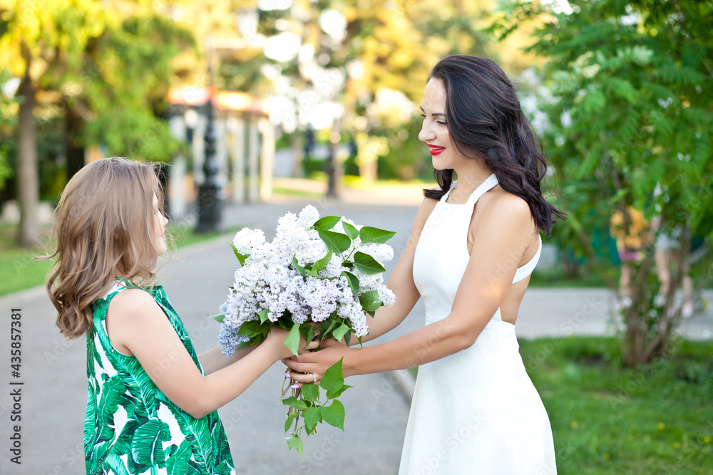 Beautiful brunette woman mom with her daughter walking in the park or spring garden among the blooming lilacs