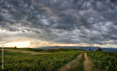 Dramatic storm scene with rain at the horizon and rural path going towards left.