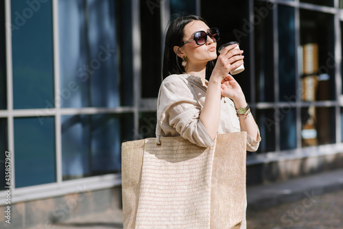 Brunette young woman with sunglasses and bag holding coffee walking in the city. Lifestyle portrait of woman © rostyslav84