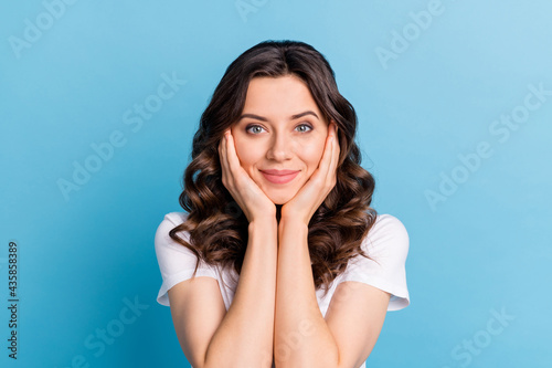 Photo of funny dreamy young woman wear white t-shirt arms cheeks smiling isolated blue color background