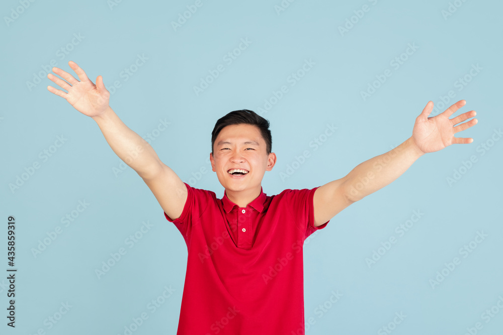 Half-length portrait of Asian young man isolated on blue studio background. Concept of human emotions Half-length portrait of Asian young man isolated on blue studio background. Concept of human emotions