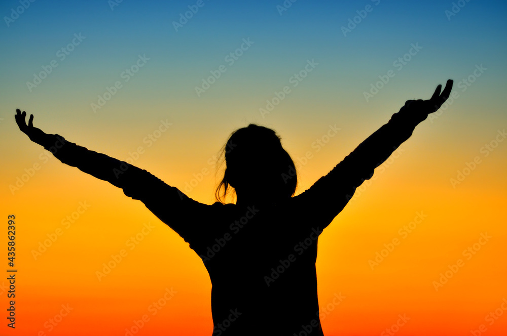 Girl silhouette raising hands in sunset light.