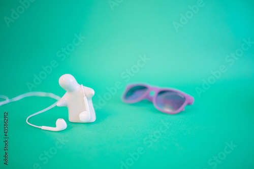 A human figure on a blue-green background with headphones and sunglasses in the background. Pastel blue background. An idea for the year.