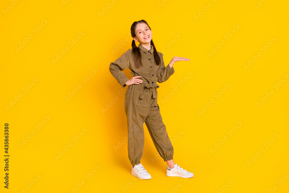 Naklejka premium Full body portrait of cheerful pupil put arm on waist palm hold show empty space isolated on yellow color background