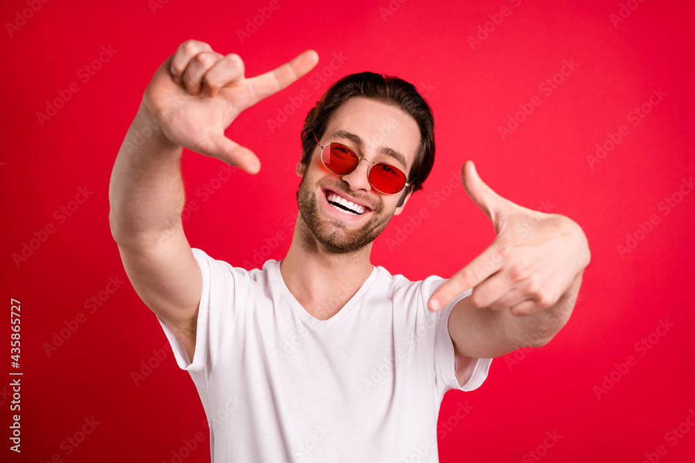 Fototapeta premium Photo of cheerful positive young man wear sunglass make fingers frame camera isolated on red color background