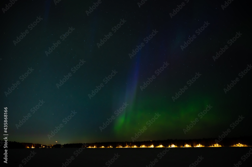 A green colour geomagnetic Aurora borealis on the starry night sky over a city. Aurora Borealis over Swedish lake Islands. Northern Sweden