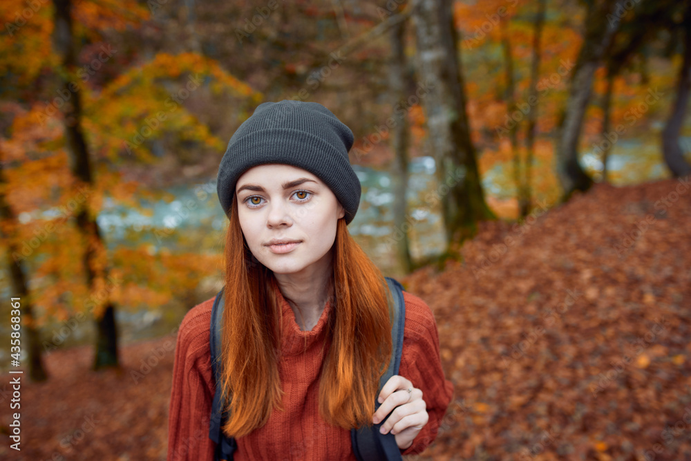 energetic woman tourist with a backpack in a red sweater and caps are resting in the autumn forest in the park energetic woman tourist with a backpack in a red sweater and caps are resting in the autumn forest in the park