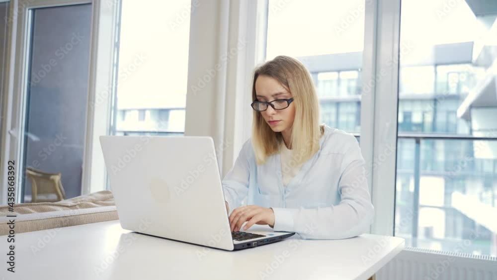 Portrait young female freelancer working on laptop or computer at home at a modern office desk. typing text. Copied or chatted. Girl student studies online remotely. Female blonde with glasses Portrait young female freelancer working on laptop or computer at home at a modern office desk. typing text. Copied or chatted. Girl student studies online remotely. Female blonde with glasses