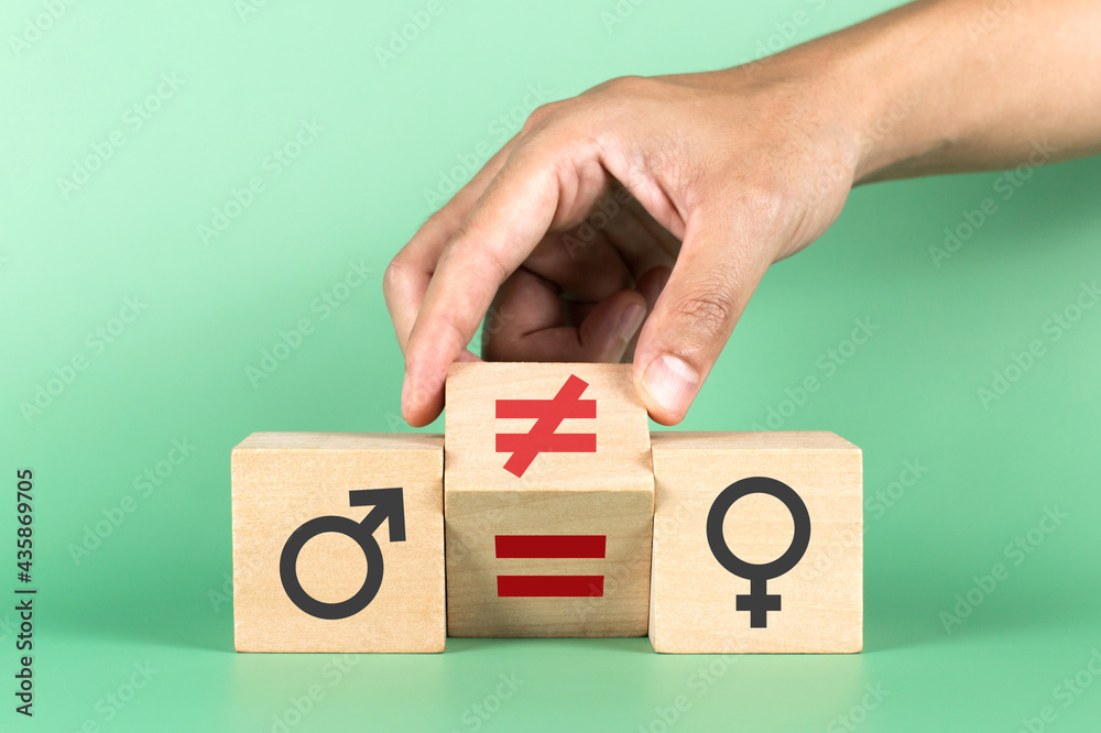 Hand flip wooden cube with symbol non-equality to equality with man and woman icons on green background Hand flip wooden cube with symbol non-equality to equality with man and woman icons on green background
