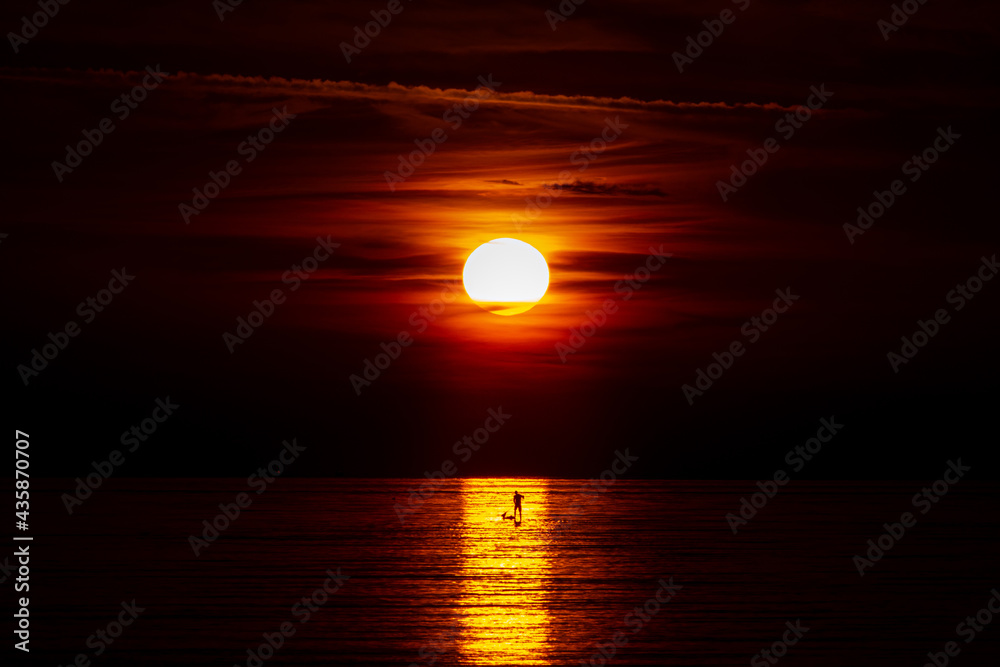 Sunrise lighting up and silhouetting a man on a paddle boat
