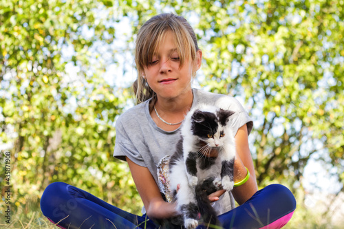 Defocus blonde little girl holding and caress cat, black and white small beautiful kitten. Nature green summer background. Girl holding and stroking pet. Love animals concept. Out of focus