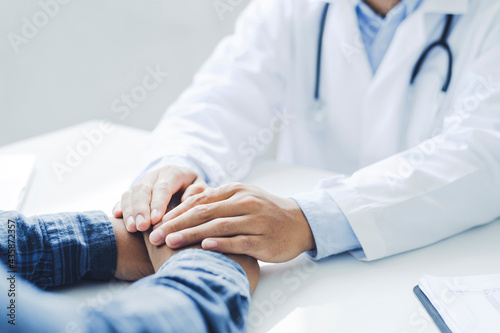 Friendly male doctor hands holding patient hand sitting at the desk for encouragement, empathy, cheering and support while medical examination. Bad news lessening, medicine and health care concept