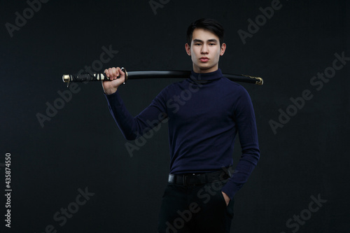 Cute Asian guy with a katana in his hands on a dark background.