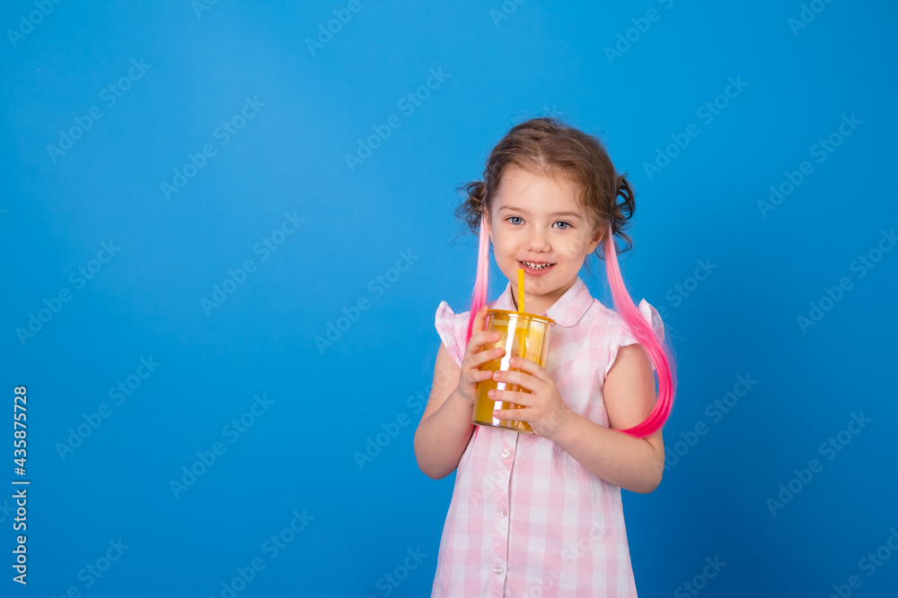 Funny child girl in pink clothes smiling holding glass of orange juice on blue background Funny child girl in pink clothes smiling holding glass of orange juice on blue background