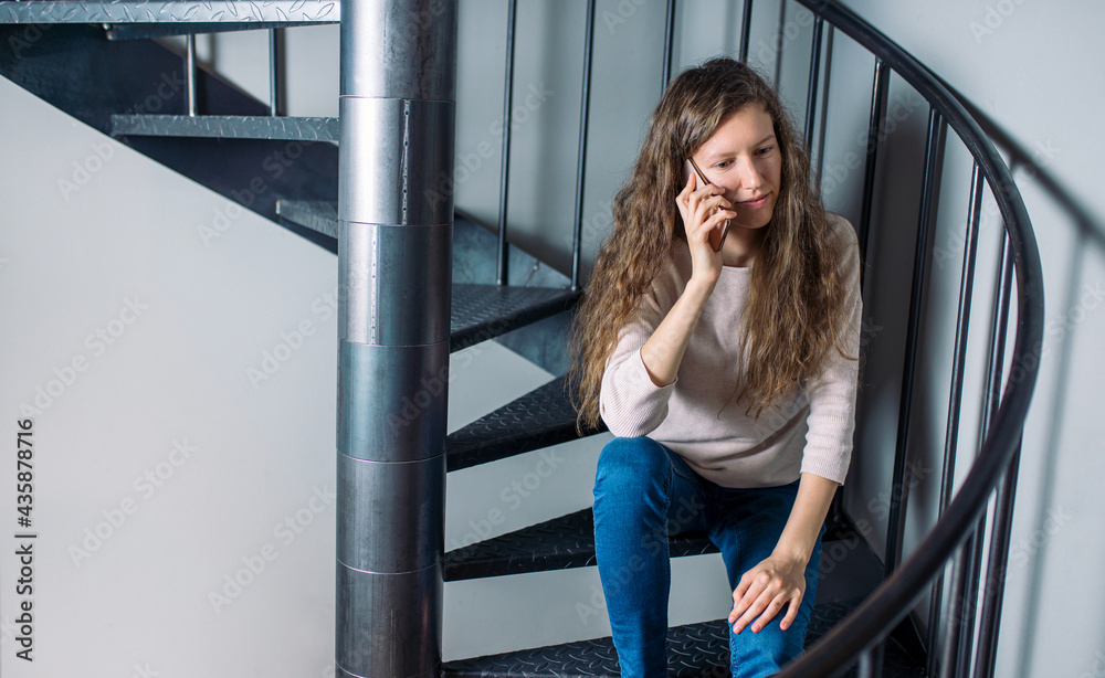 Natural looking girl casually sitting on a spiral stairs and talking on the phone. Natural looking girl casually sitting on a spiral stairs and talking on the phone.