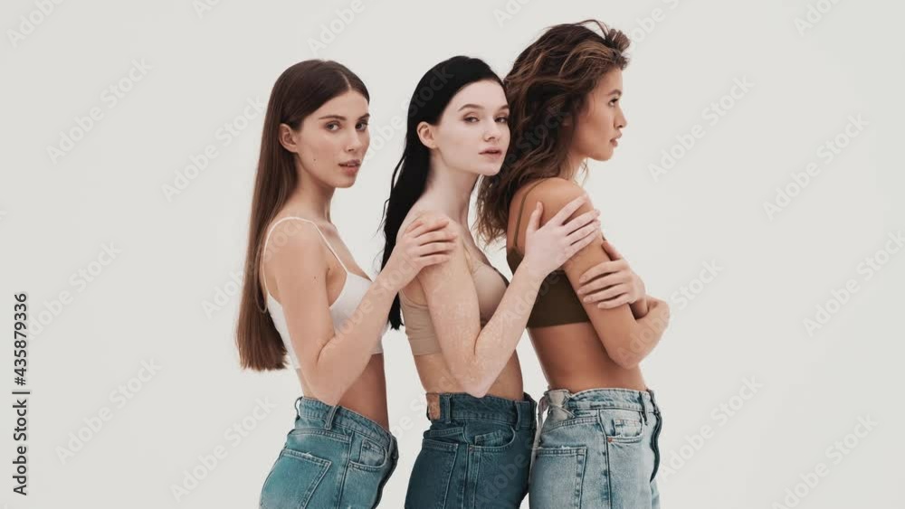 The side view of three girls holding each other's hand on the shoulder and turning to the camera in a white studio The side view of three girls holding each other's hand on the shoulder and turning to the camera in a white studio