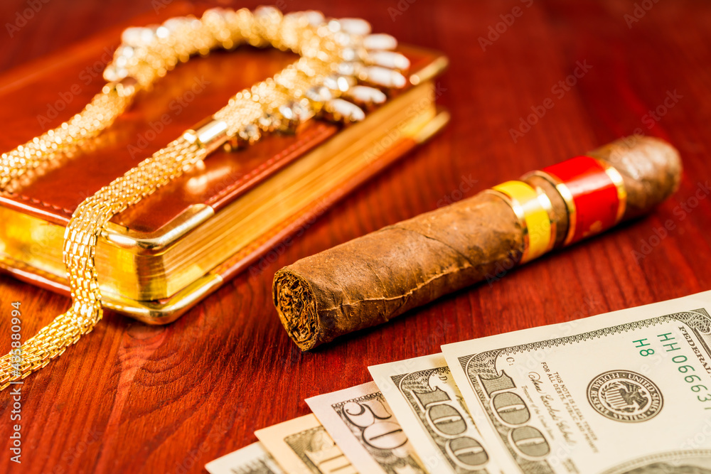 Money with a leather diary and cuban cigar with jewellery on a mahogany table Money with a leather diary and cuban cigar with jewellery on a mahogany table
