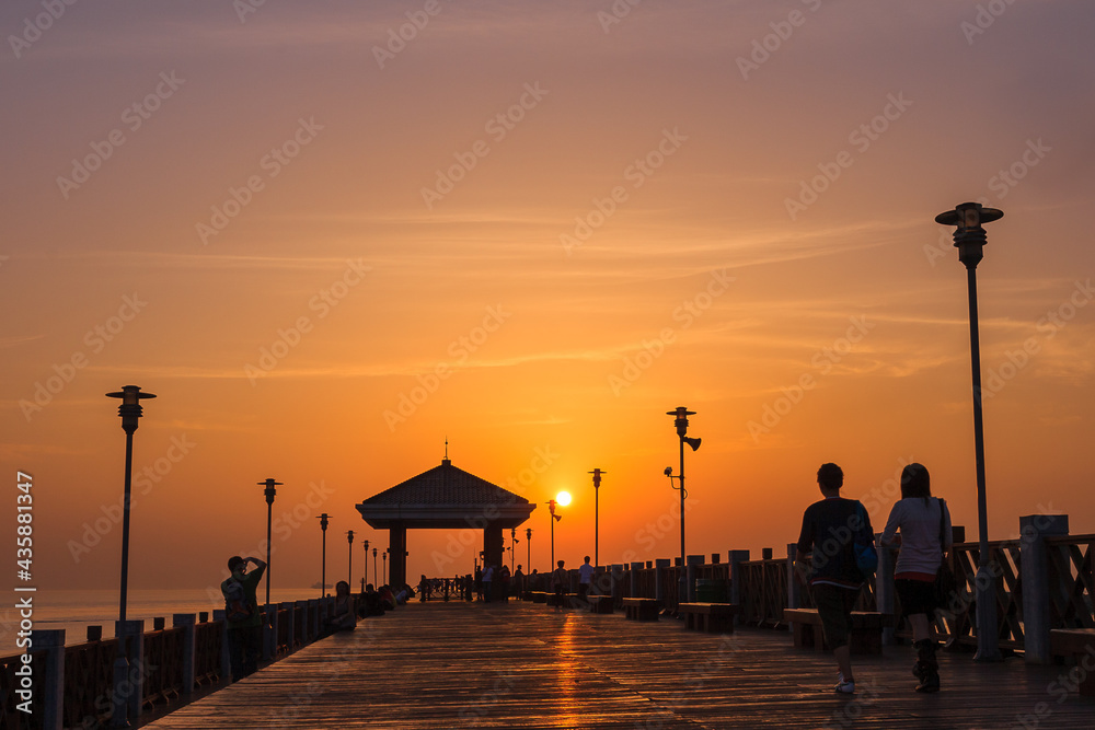People take a leisurely stroll on a wooden plank road by the sea at a romantic moment when the sun is setting