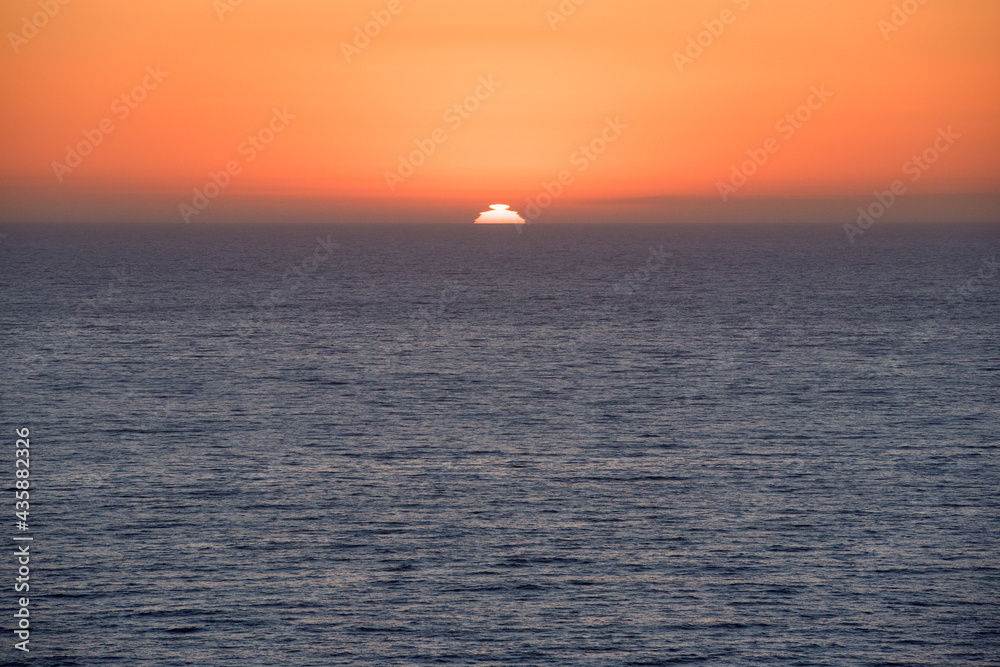 Sunset over the ocean horizon with bright orange sky