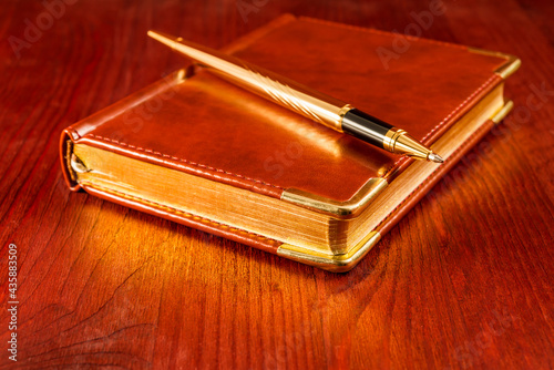 Golden pen on a leather diary on a mahogany table